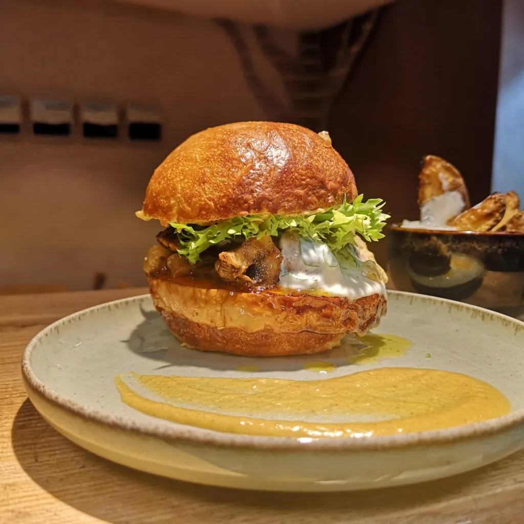 Un burger végétal maison : brioche dorée, légumes rôtis, sauce aux herbes et potatoes